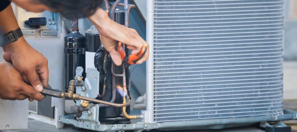 Close-up of a technician working with a tool on an air conditioning unit's compressor components