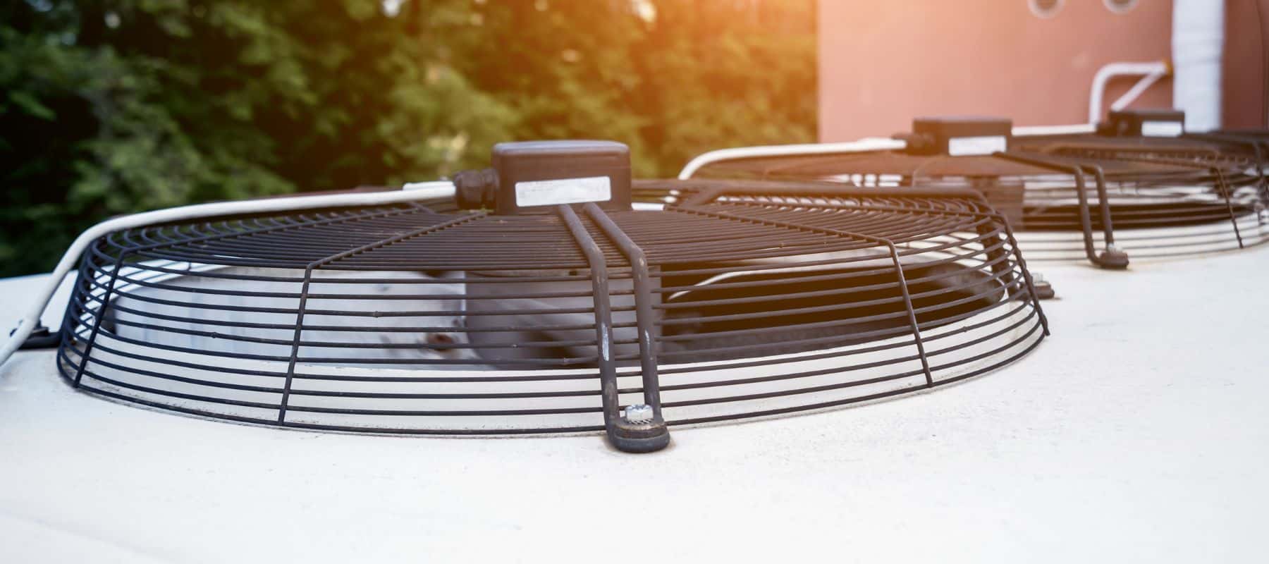 Two circular cooling fans on rooftop air conditioning units with sunlight filtering through the surrounding trees